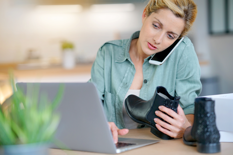 Woman on laptop and mobile phone holding shoes purchased online