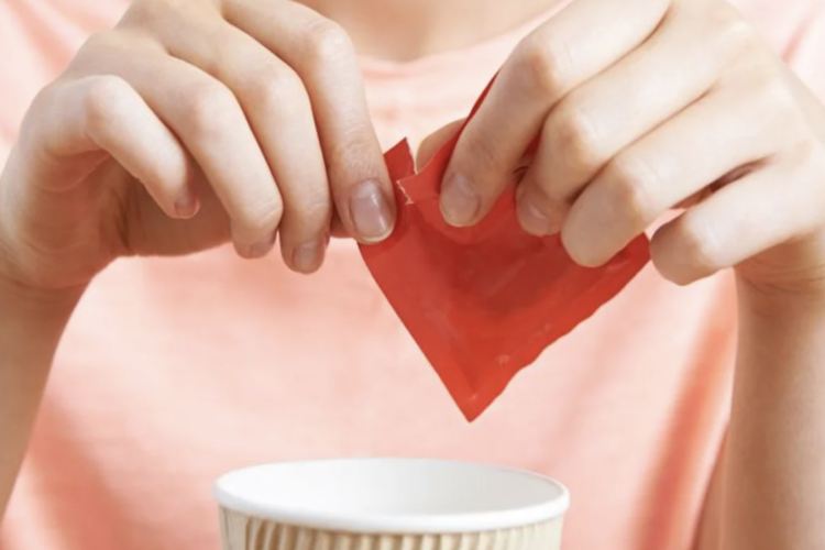 Person opening a sugar packet to add to a cup of coffee