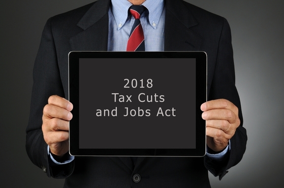 Businessman holding a tablet that says "2018 Tax Cuts and Jobs Act."