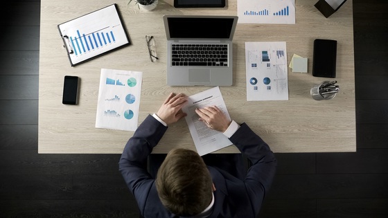 Overhead shot of procurement manager at desk with computer and papers with charts and graphs