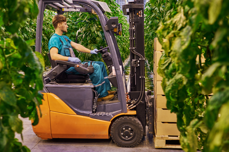 A forklift driving past greenery