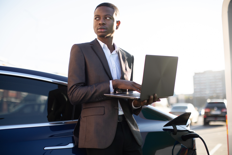 Man holding a laptop while his EV charges