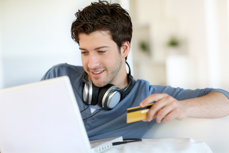 Young man with headphones around his neck holding a credit card and doing online shopping