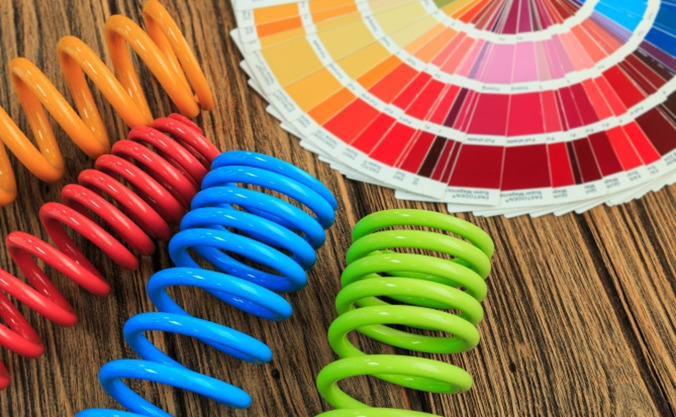 Orange, red, blue, and green powder coated metal car spring parts with fanned out color chart on a wooden background.