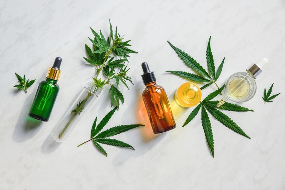 Various glass bottles with CBD oil, THC tincture, and hemp leaves. 
