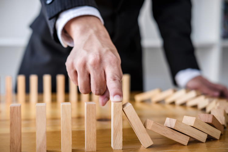 Businessman's hand stopping falling wooden dominoes effect from continuous toppled or risk