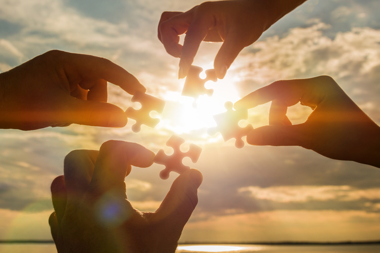 Hands holding puzzle pieces with sunrise in the background