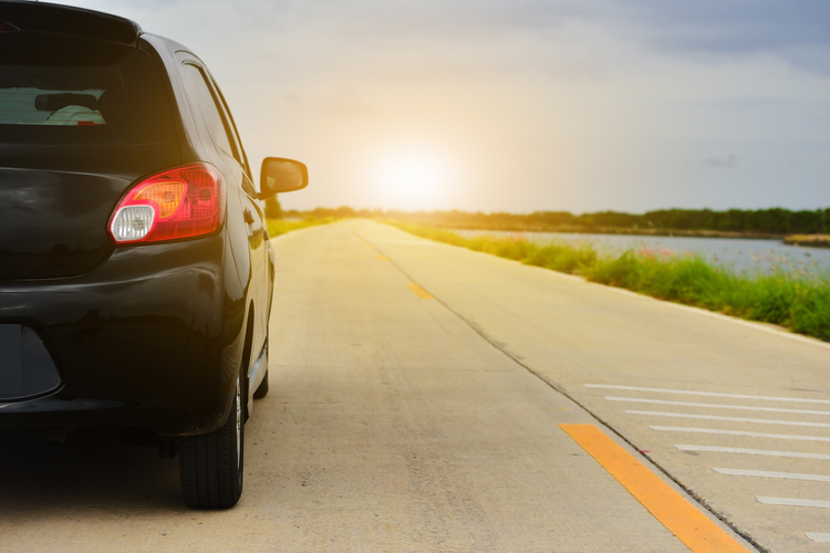 Car parked on road with sun and open highway in background.