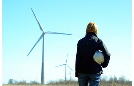 Women engineer with white safety hat standing in a field with wind turbines in the background