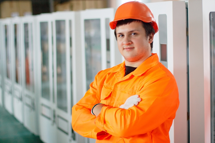 Industrial worker in orange uniform and hard hat standing in front of row of vending machines