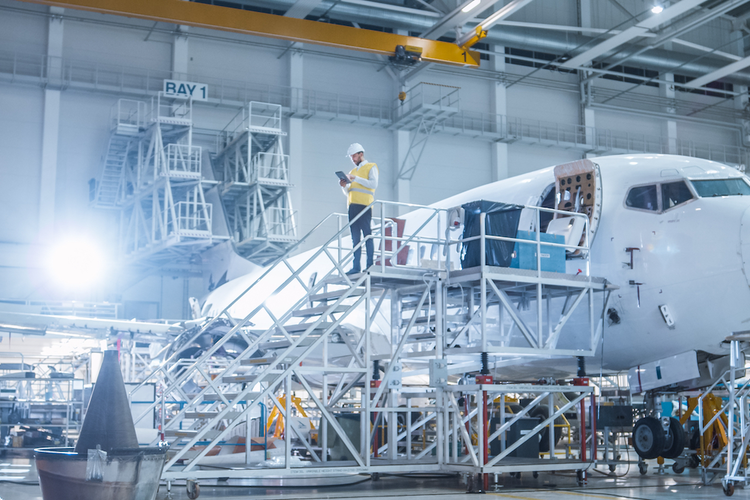 Worker standing next to airplane in hangar