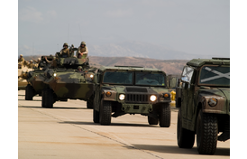 Marines in armored military trucks driving down a road