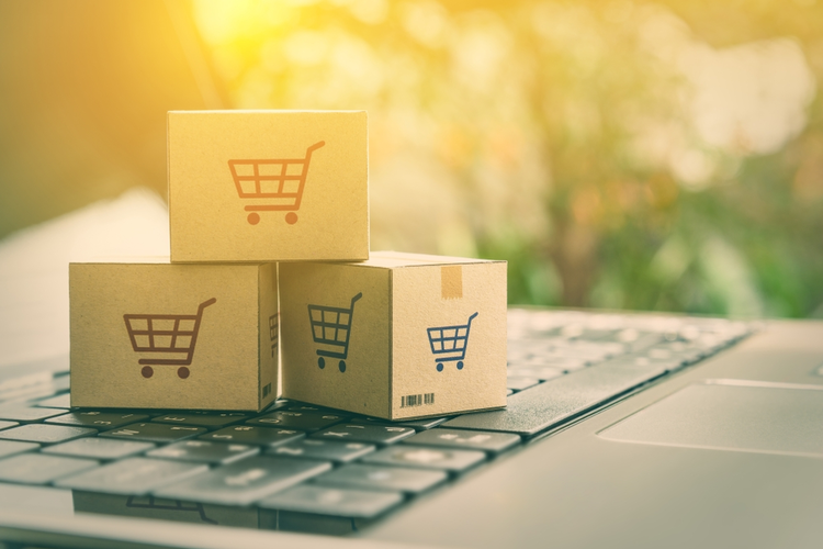 Online shopping/e-commerce and delivery service concept: Paper cartons with a shopping cart on a laptop keyboard.